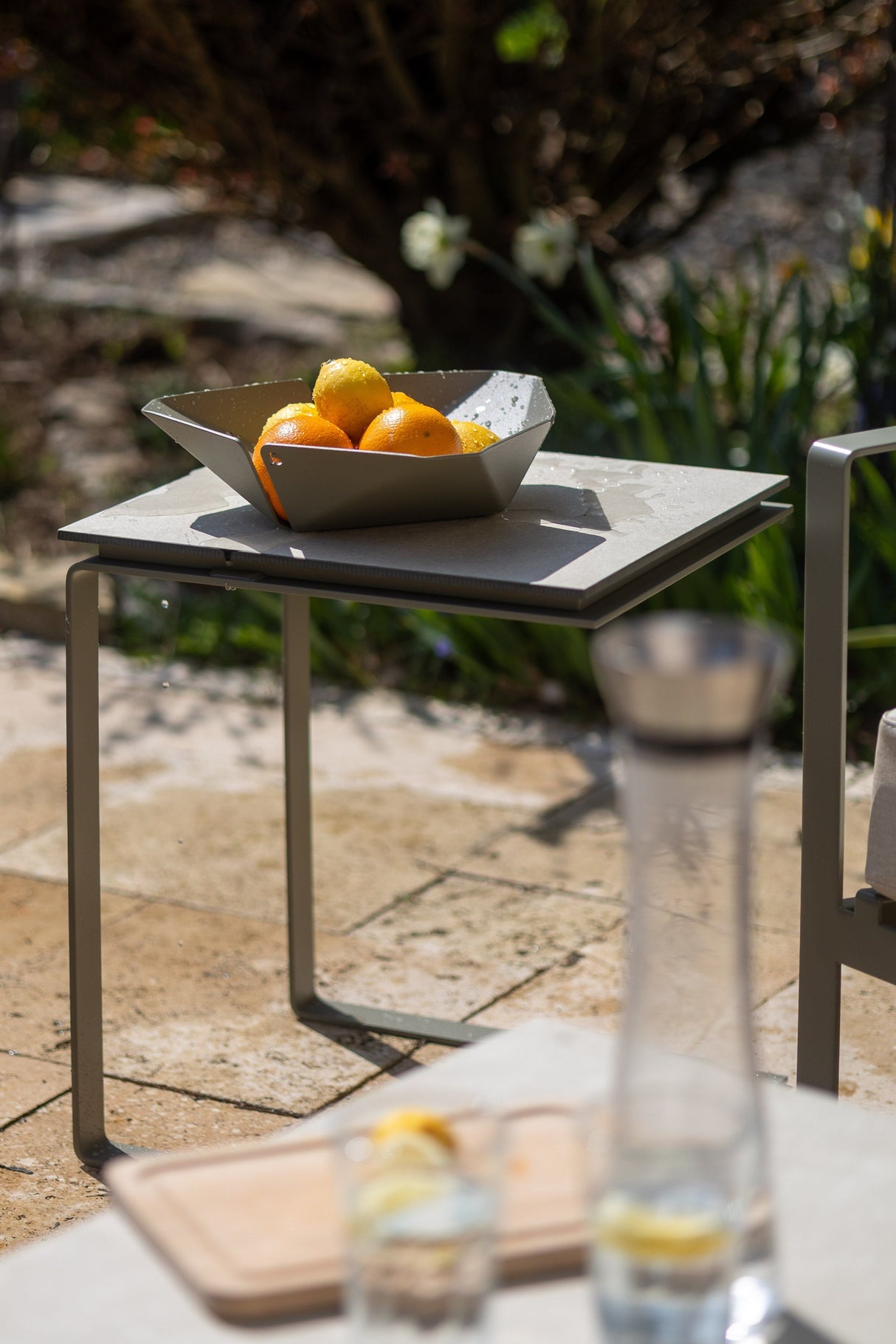 Moderner ALTO Beistelltisch aus Edelstahl, pulverbeschichtet, im Garten mit Obstschale dekoriert – wetterfest und elegant.