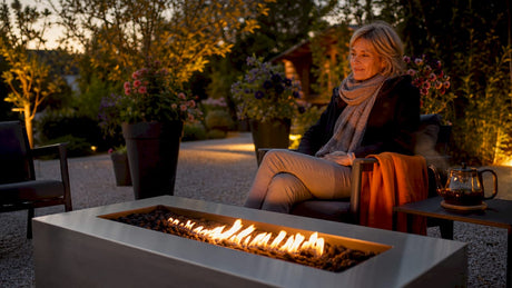 Eine Frau genießt an einem gemütlichen Abend die wohlige Wärme ihres Gartenfeuers.