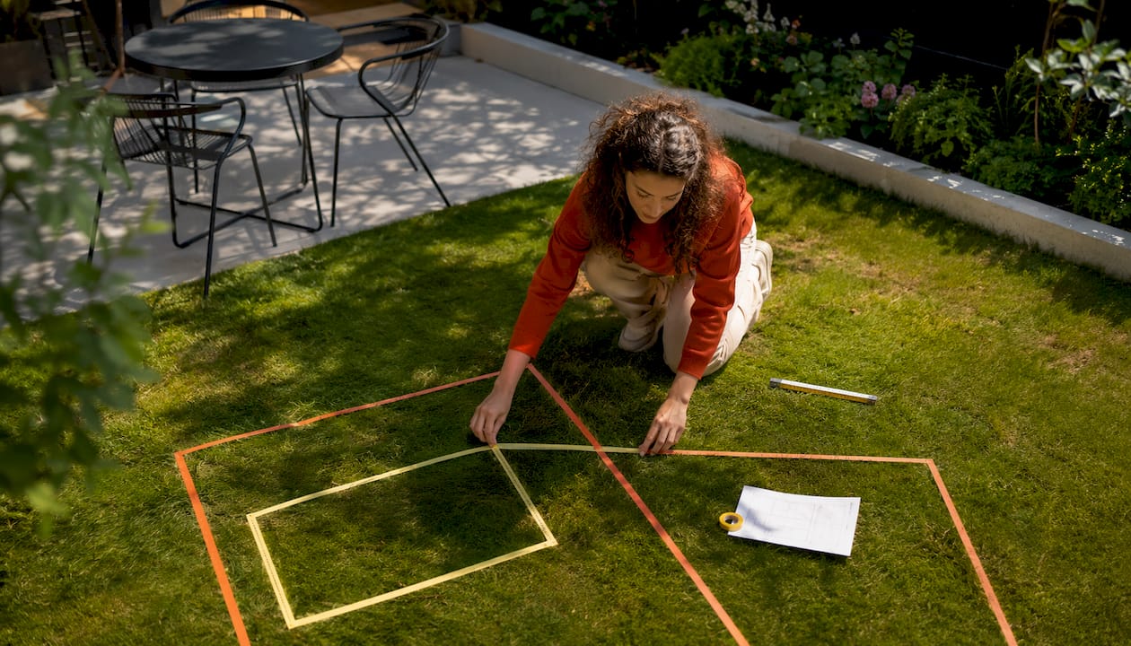 Eine Frau markiert mit Klebeband die geplante Anordnung ihrer Gartenmöbel auf der Terrasse.