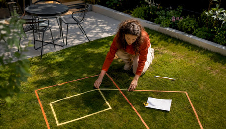 Eine Frau markiert mit Klebeband die geplante Anordnung ihrer Gartenmöbel auf der Terrasse.