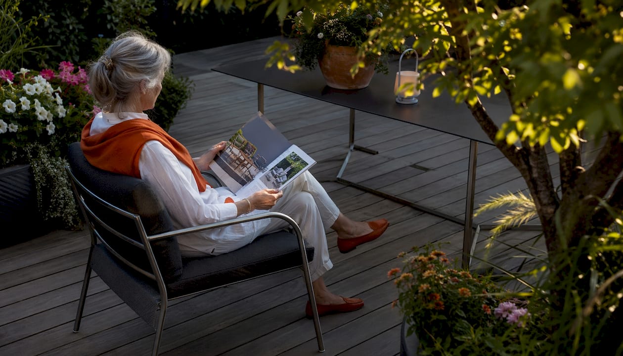 Eine Frau genießt die Sonne auf einem liebevoll gefertigten Gartenstuhl inmitten ihres Gartens.